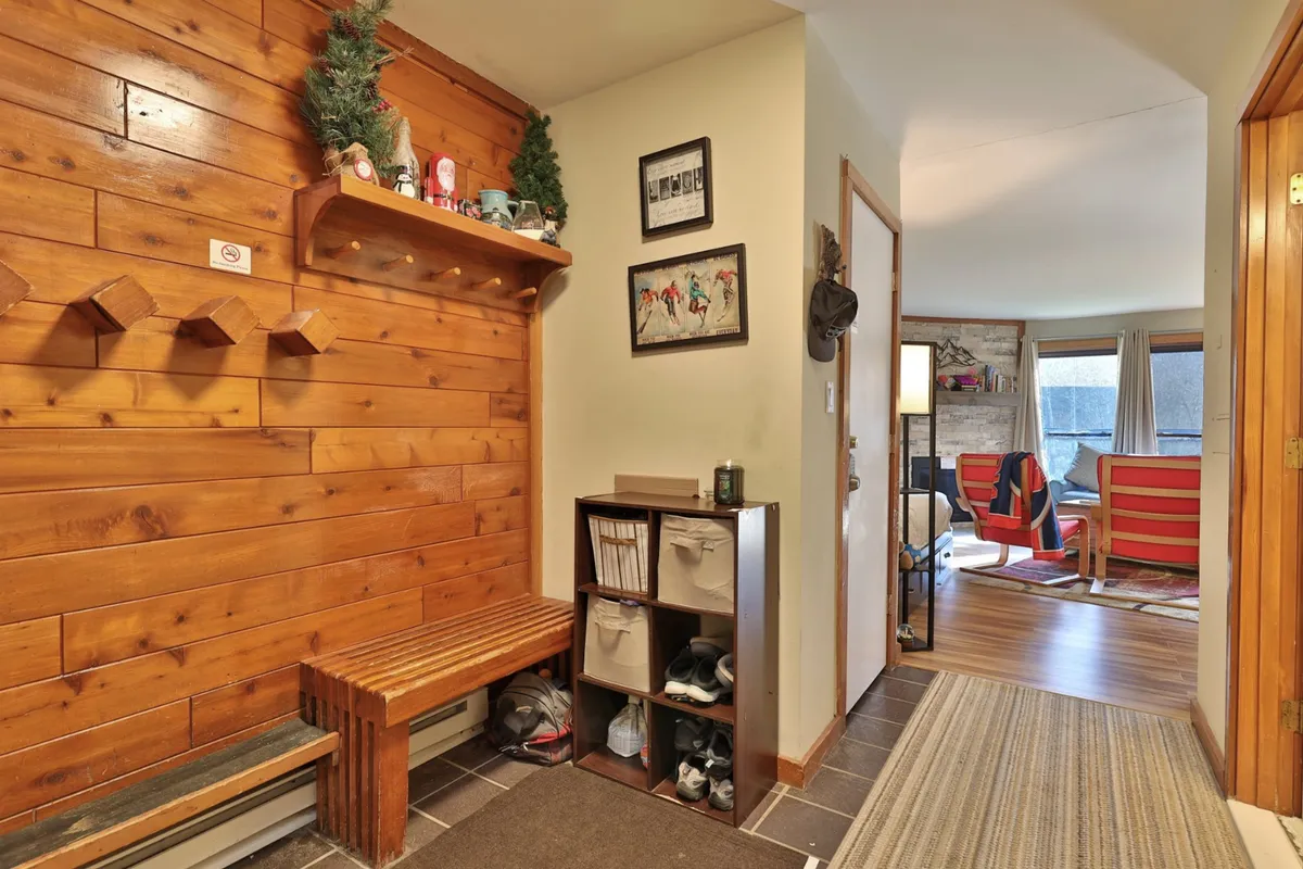 A welcoming interior entryway featuring a wooden wall, a bench for sitting or removing shoes, a shelf with decorative items, and a storage unit for outdoor gear. The cozy mood and practical layout suggest a seamless transition from the outside world into a private retreat.