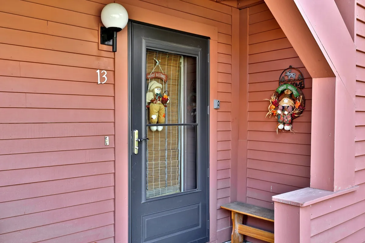 An inviting exterior view of the condo’s front door, complete with decorative dolls, a light fixture, and a wooden bench on the porch. The coziness is enhanced by subtle seasonal decorations, setting a welcoming tone for families arriving to start their adventures.
