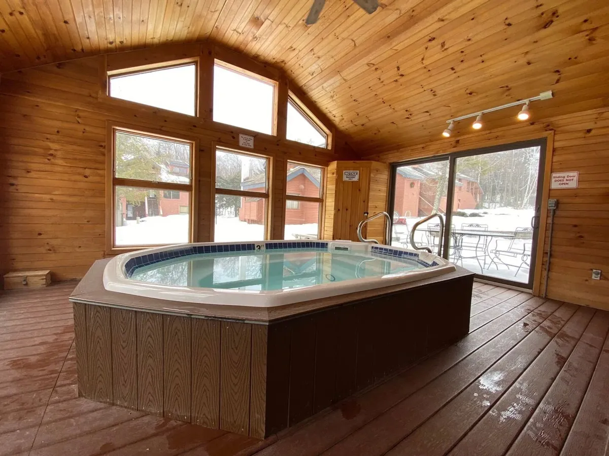A cozy indoor hot tub area with large windows and a wooden ceiling, inviting guests to soak and relax while enjoying views of the snowy outdoors. The mood is serene and perfect for après-ski or unwinding after a day of adventure.