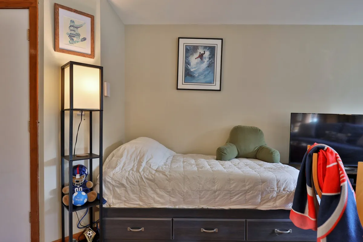 A welcoming room featuring a bed, lamp, artwork, TV, and a stuffed animal. The space exudes comfort and is well-suited for both relaxation and entertainment.