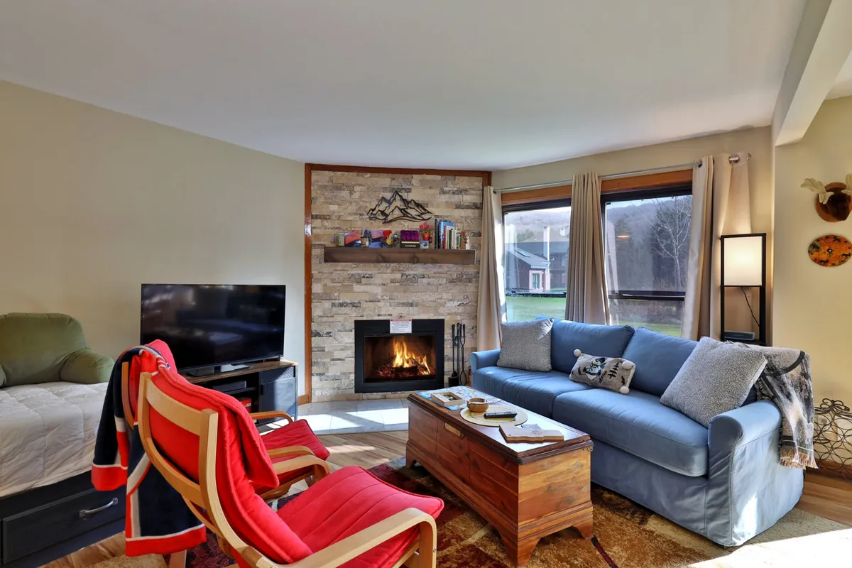 The interior image showcases a warm, inviting living area centered around a crackling fireplace. A plush sofa faces the hearth, flanked by a bookshelf and a television, creating the perfect setting for relaxing evenings. The ambiance is cozy and intimate, ideal for unwinding after a day on the slopes or enjoying quiet moments with loved ones.