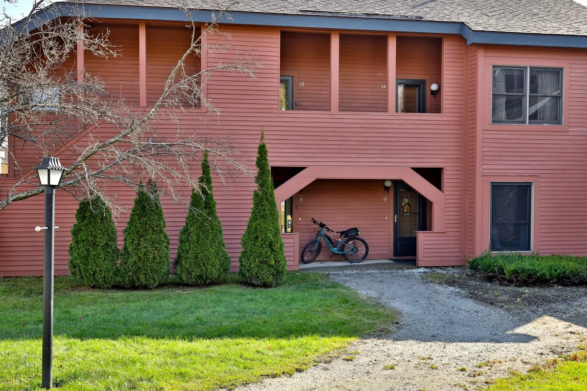 The inviting pink exterior of the condo building, surrounded by green shrubs and featuring a bicycle parked outside. The scene suggests outdoor activities like cycling, gathering with neighbors, and enjoying sunny afternoons in a friendly neighborhood.