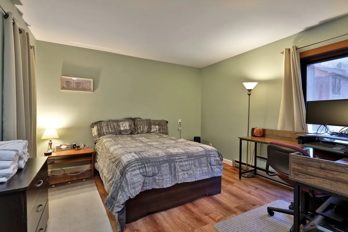 A cozy corner featuring a neatly made bed, a functional desk by the window, a lamp, and natural light streaming in. This nook is inviting for reading, working remotely, or resting, and hints at the flexibility provided by the twin bed in the living room.