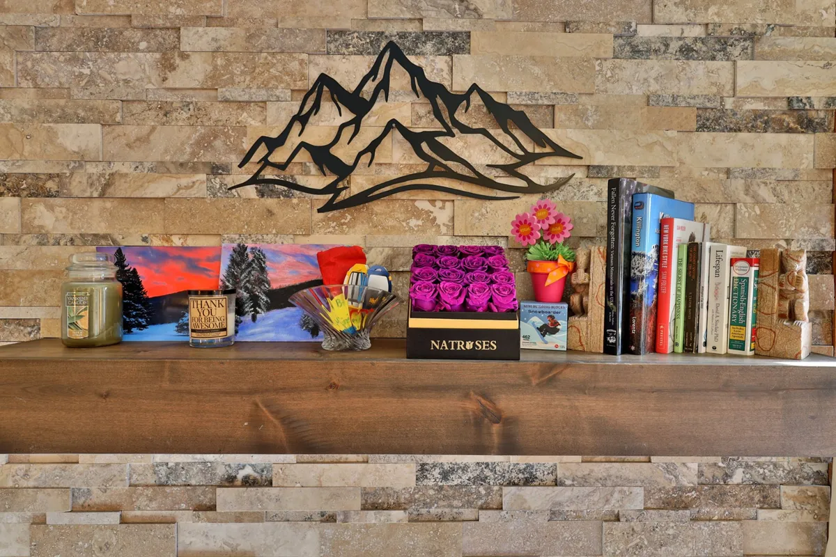 An inviting living area with mountain-themed wall art, a vibrant flower arrangement, a filled bookshelf, and candles. The space is designed for activities such as reading, writing, or simply relaxing, with a creative and tranquil atmosphere.