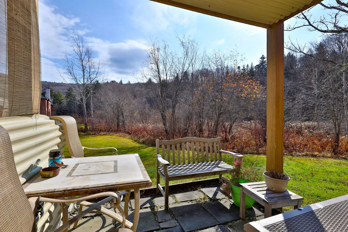 An exterior scene featuring a wooden bench and a stone table set amidst lush green trees and an open field. The tranquil space is ideal for relaxing outdoors, enjoying coffee, reading, or birdwatching, with natural scenery that invites exploration and contemplation.