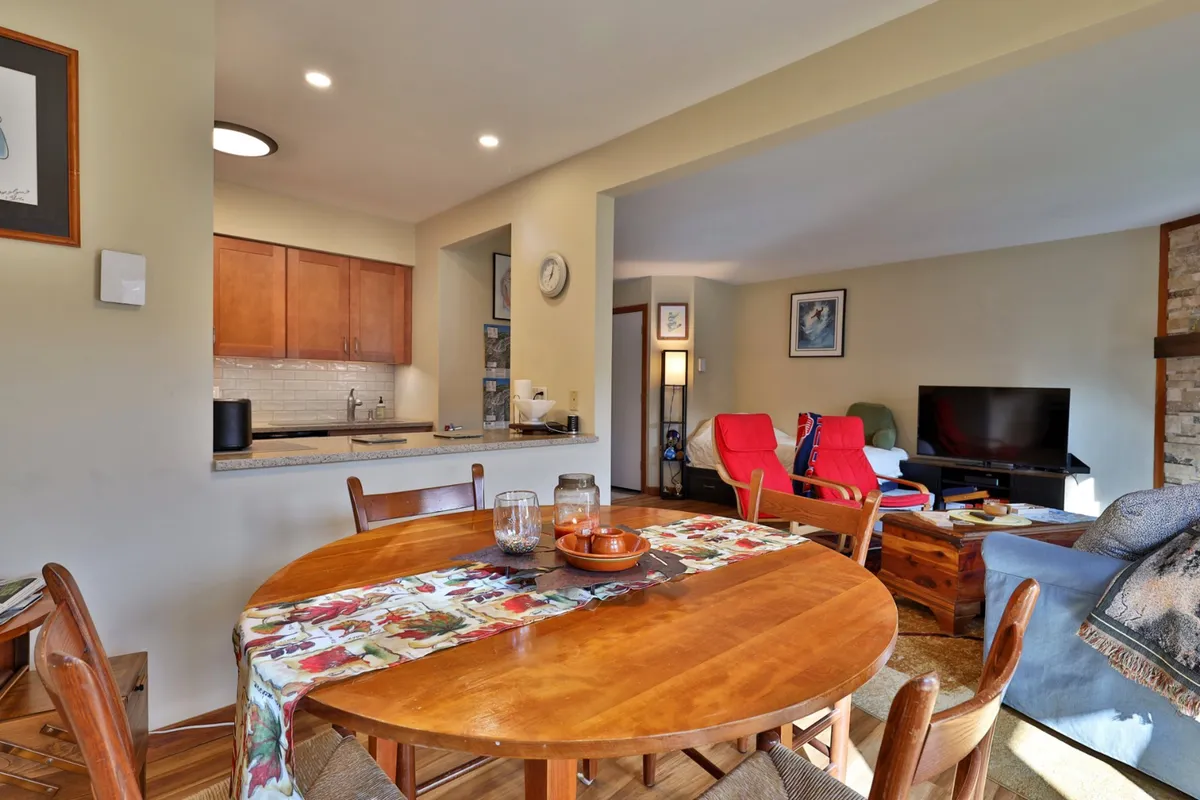 A broad interior shot capturing the dining table, adjacent kitchen area, living room seating, and artwork on the walls. The open layout highlights spaces ideal for family meals, casual gatherings, and cozy relaxation after a day outdoors.