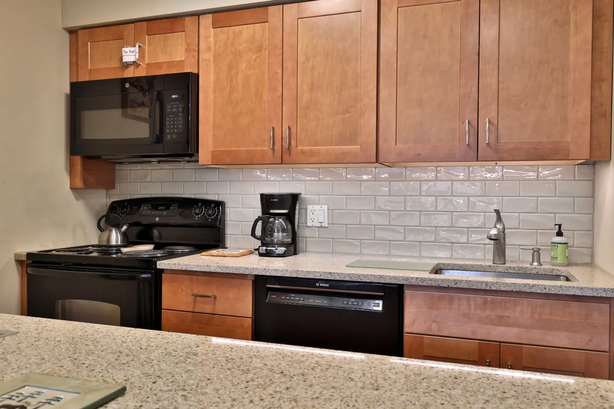 A bright, welcoming kitchen featuring modern appliances including a refrigerator, microwave, and dishwasher. The granite countertop and wooden cabinets create a functional and stylish space for cooking and preparing meals. Natural light streams in, highlighting the clean lines and inviting atmosphere.