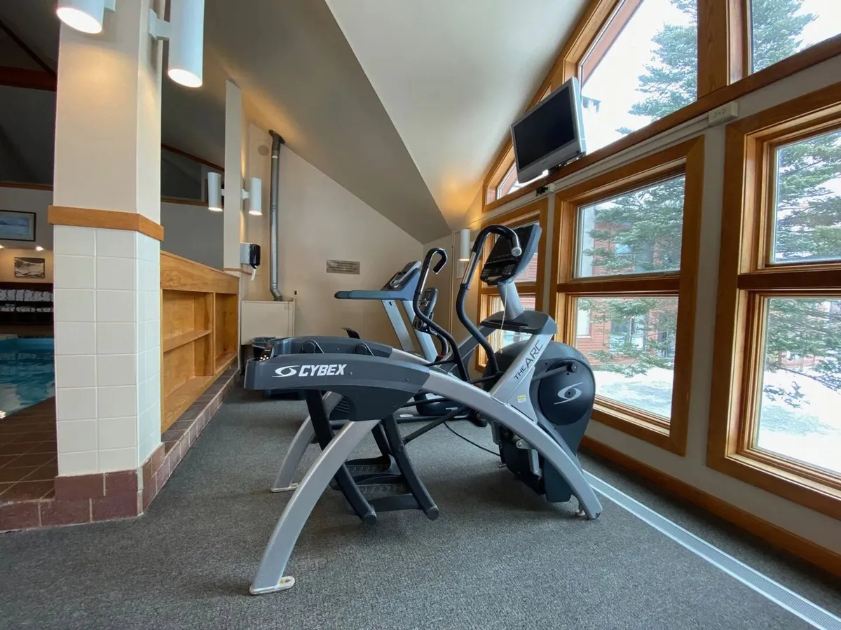 A bright fitness area featuring elliptical machines positioned near large windows, with a TV overhead. The space is modern and motivational, offering views outside and an opportunity to stay active even on rainy days.